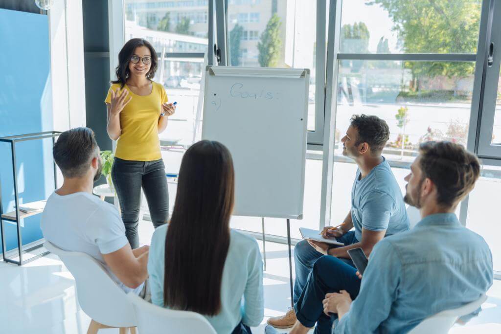 Photograph of woman leading meeting and working on whiteboard