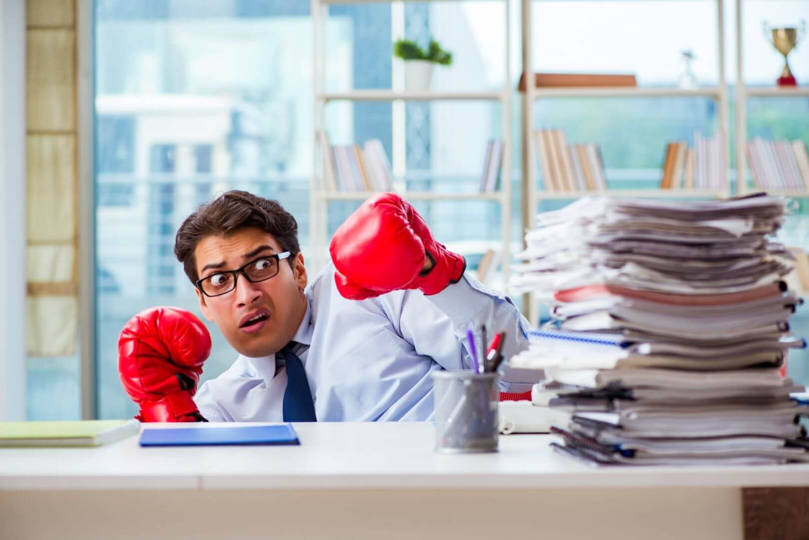 Silly photograph of man with boxing gloves looking intimidated by imposing stack of paperwork