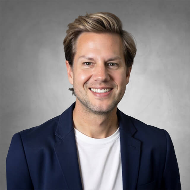 Headshot of a person wearing a collared shirt and a jacket in front of a gray background.